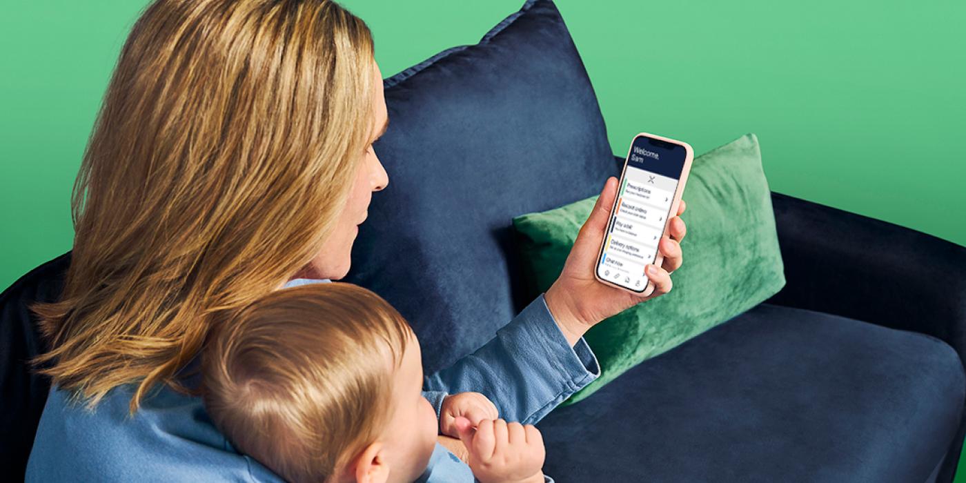 A mother holds a baby while looking at her smartphone.