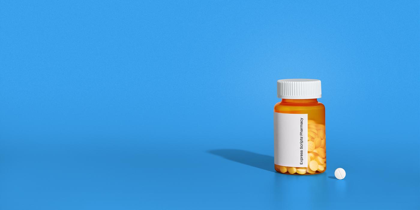 A prescription bottle sits on a counter next to a small pill.