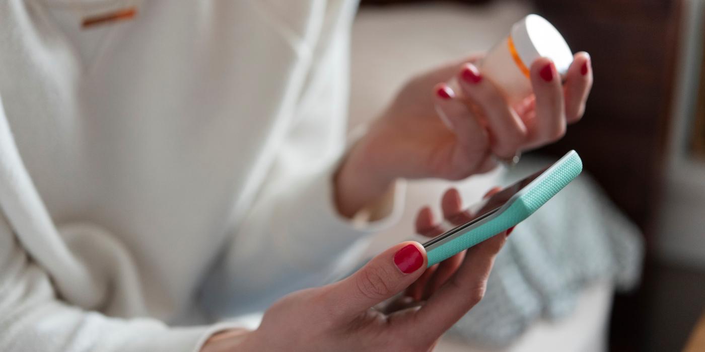 woman holding medication while on mobile phone