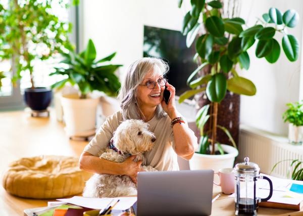 woman speaking on cellphone in front of computer with dog in lap