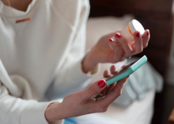 woman holding medication while on mobile phone