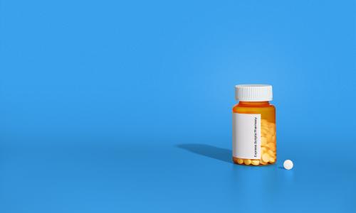 A prescription bottle sits on a counter next to a small pill.