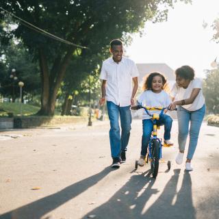 Couple helping child ride a bike.