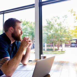 young adult man sitting with laptop thinking