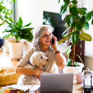 woman speaking on cellphone in front of computer with dog in lap