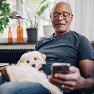 retired man sitting holding mobile phone with dog on lap